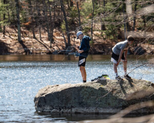Two boys fishing from a large rock at the edge of Clamshell Pond