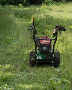A brush cutting machine temporarily parked along a trail it has cut through tall grass.