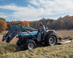 Closeup of a blue tractor and driver mowing a field in autumn